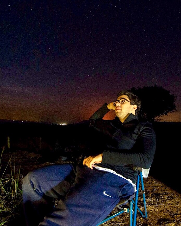 Luis Colaferro sitting in a camping chair at night, looking at the starry sky